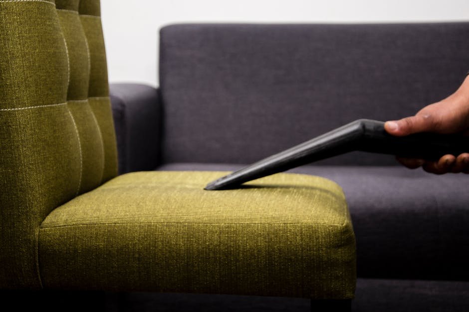 A pristine, white upholstered sofa with button-tufted backrest and rolled arms, positioned against a white paneled wall in a well-lit room. The sofa features padded seat cushions and dark wooden legs,